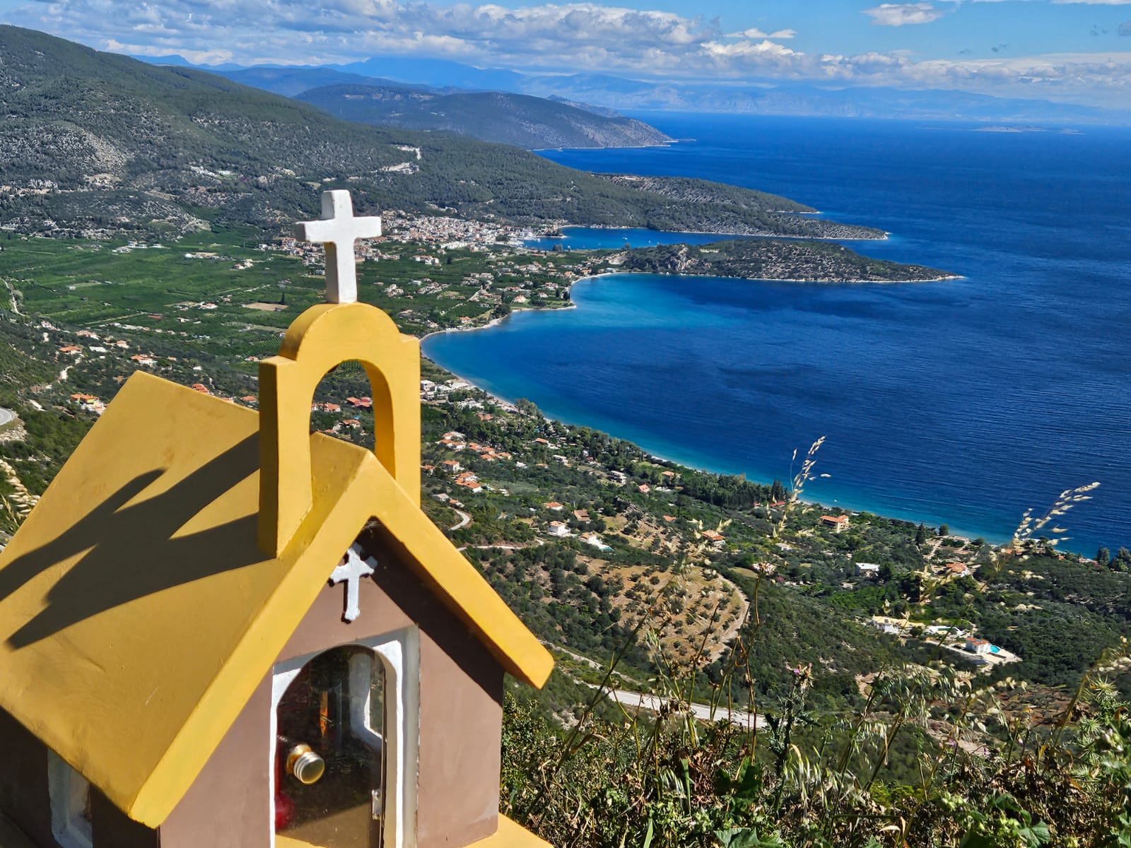 Panoramic view of the Saronic Gulf and eastern Peloponnese coast with a small yellow chapel in the foreground